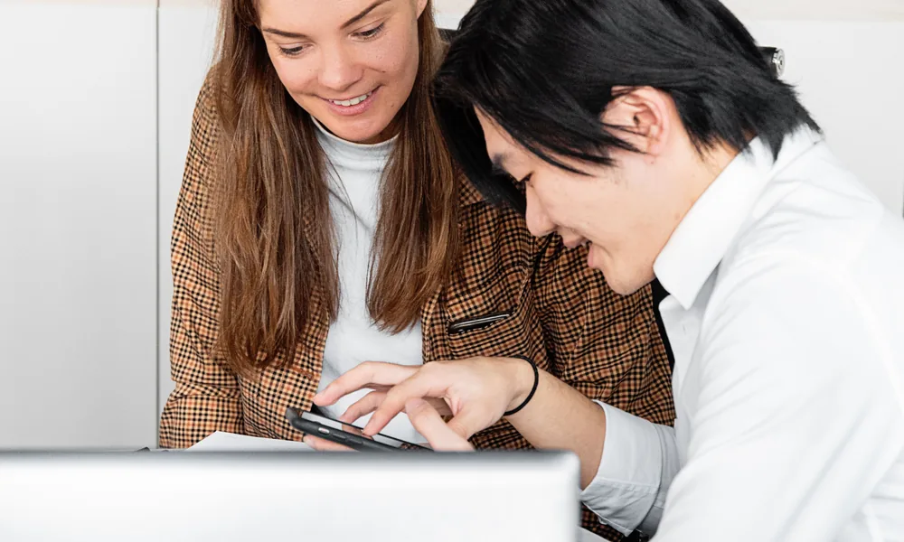Colleagues reviewing mobile information on a laptop and smartphone
